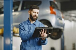 Smiling auto mechanic uses digital tablet in car repair shop environment.